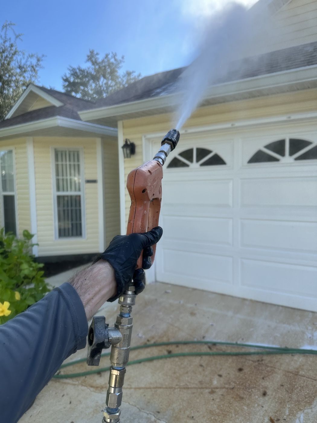 Pressure washing a garage door and driveway at a single-story home