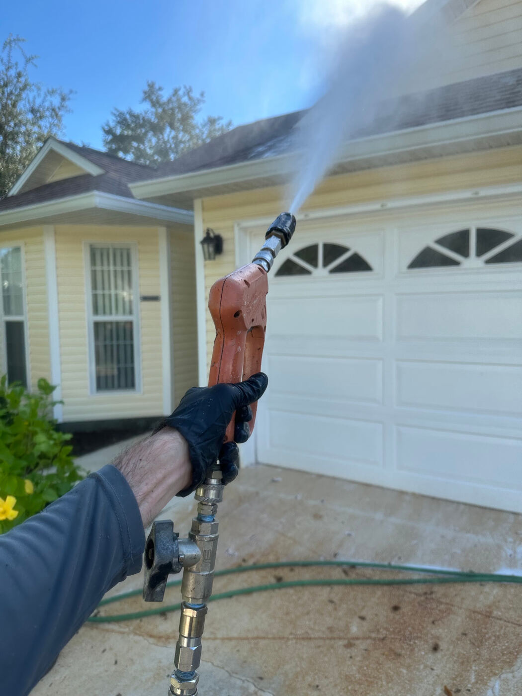 Gulf Coast Detailers pressure washing the roofline above a garage door at a single-story home